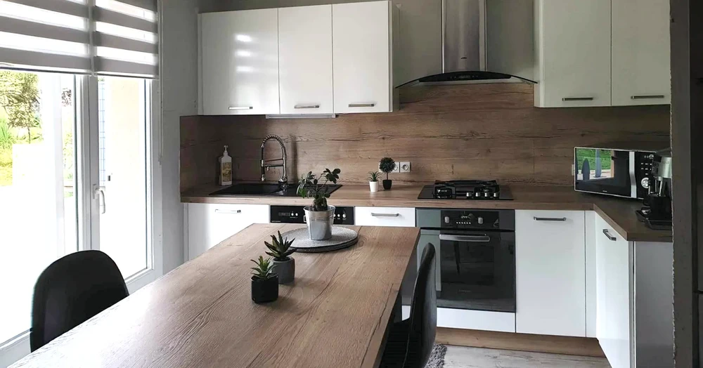 Cuisine moderne avec îlot central en bois, chaises noires, personne préparant à manger